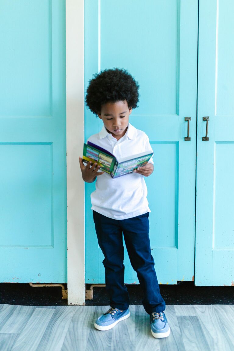 Charming scene of a young boy immersed in reading a book, standing by turquoise doors indoors.